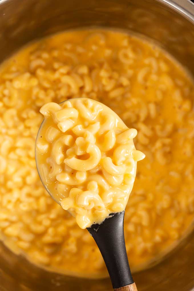 A serving spoon lifting mac and cheese from a pressure cooker.