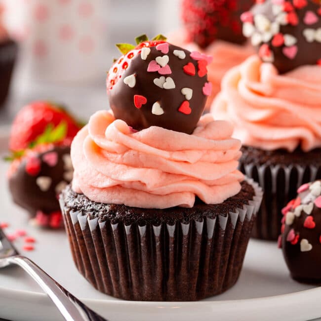 Chocolate cupcakes covered with strawberry frosting and a chocolate covered strawberry