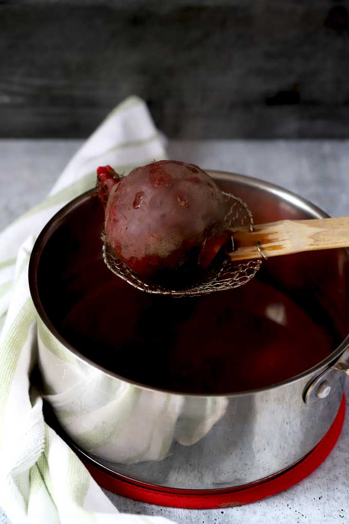 Lifting a boiled beet from a pot.