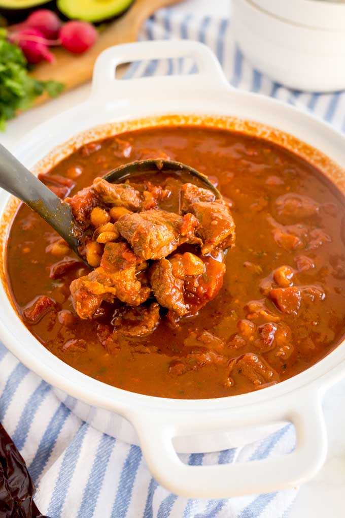 A pot filled with Pork Pozole getting scooped with a soup ladle