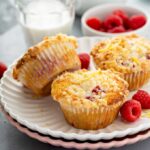 Three raspberry muffins with buttery lemon crumb topping on a plate