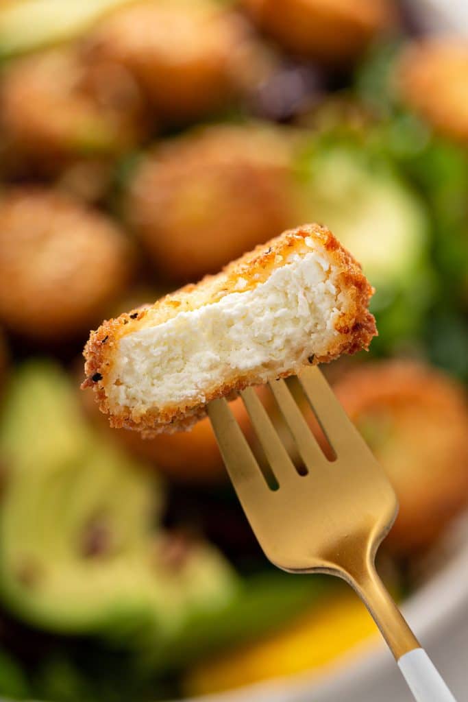 Close up of fried goat cheese cut in half and showing the creamy interior and the crispy coated exterior.