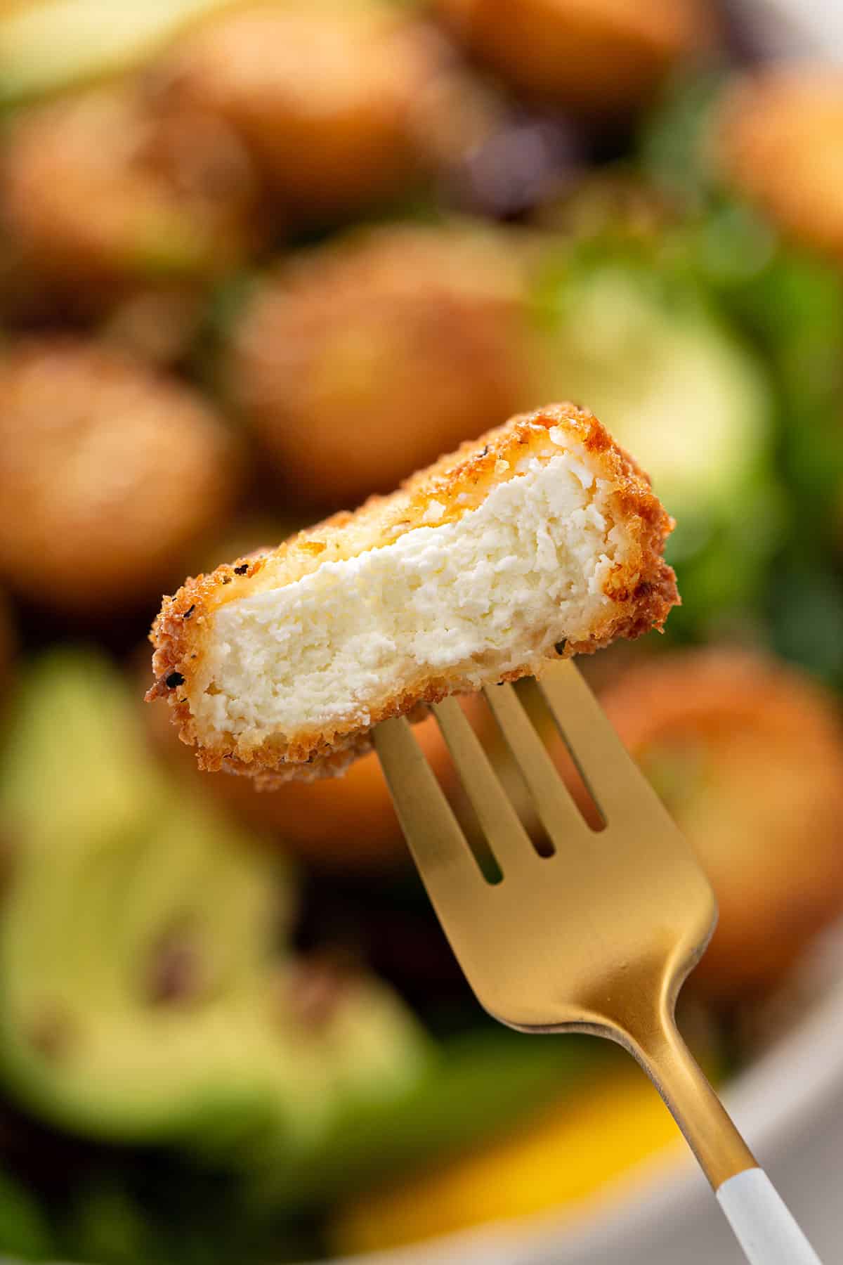 Close up of fried goat cheese cut in half and showing the creamy interior and the crispy coated exterior.