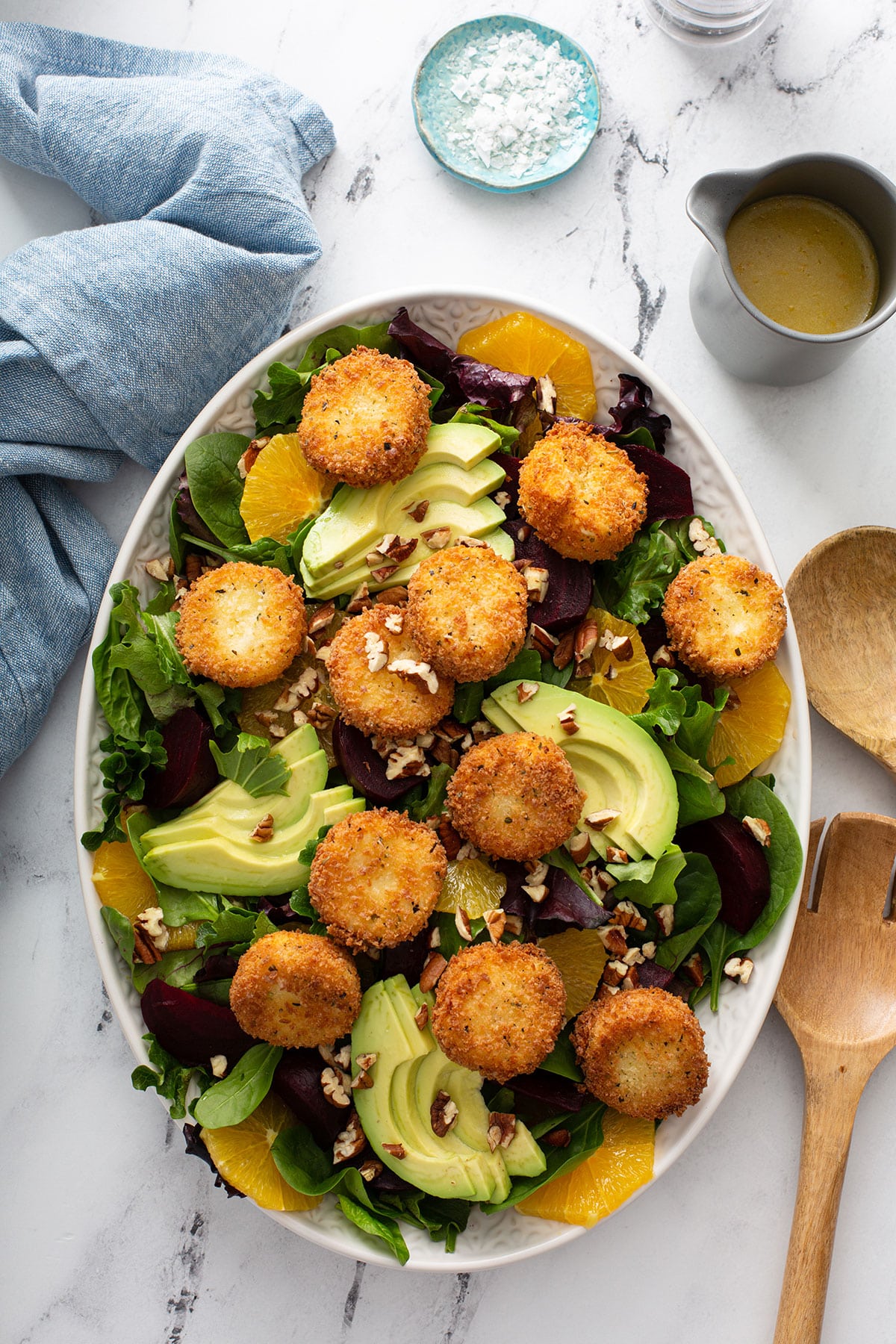 top view of Roasted Beet salad topped with crispy goat cheese and avocado slices on a white platter.