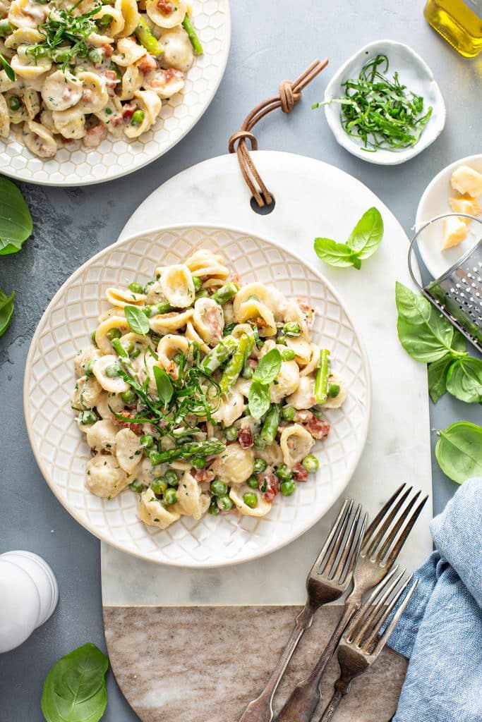 A couple of plates with creamy pasta with asparagus and peas.
