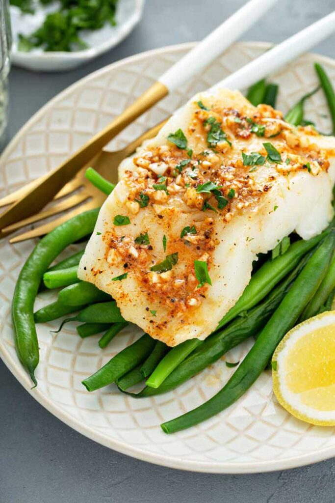 A fillet of baked cod with Cajun butter on a bed of blanched green beans