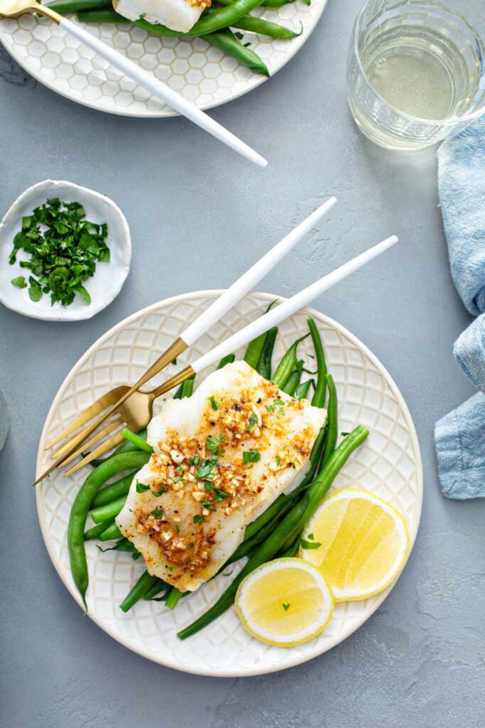 A plate with a fillet of baked cod over green beans topped with Cajun butter