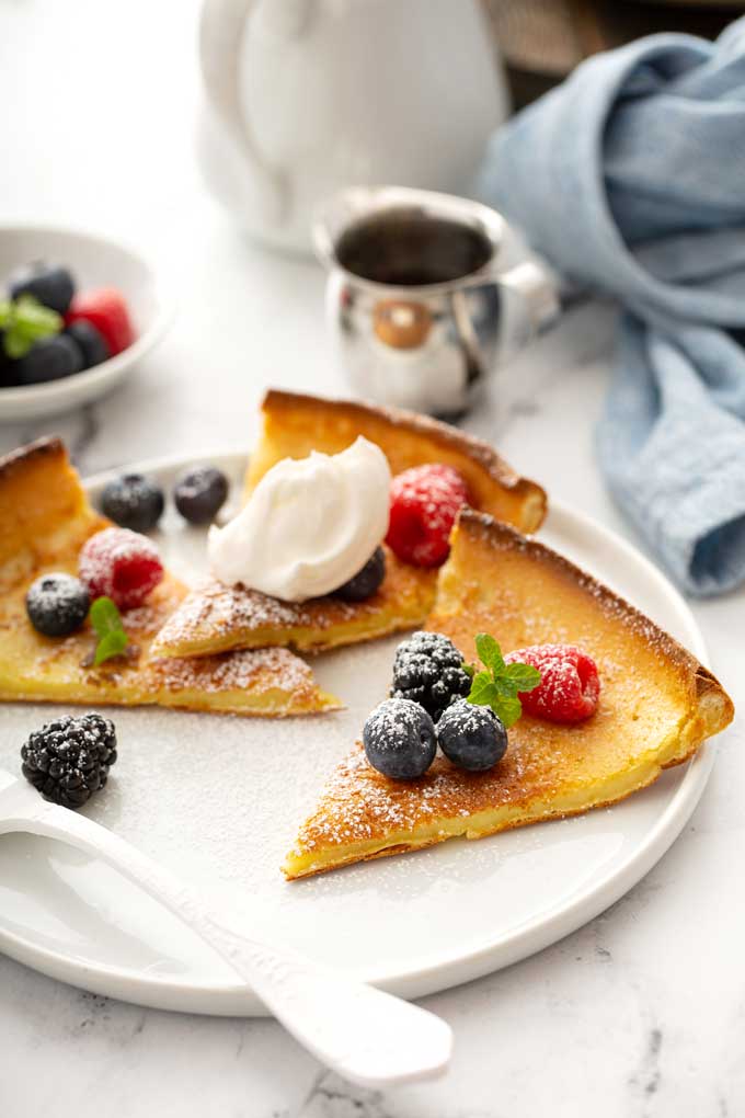 Slices of Dutch baby pancake topped with powdered sugar, berries and whipped cream