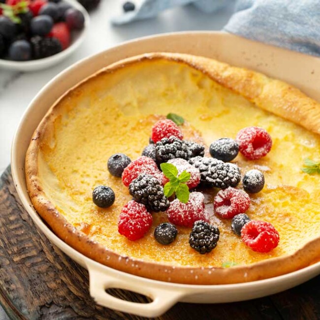 a dutch baby pancake topped with berries and powdered sugar