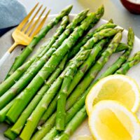 Cooked asparagus served with lemon on a plate.