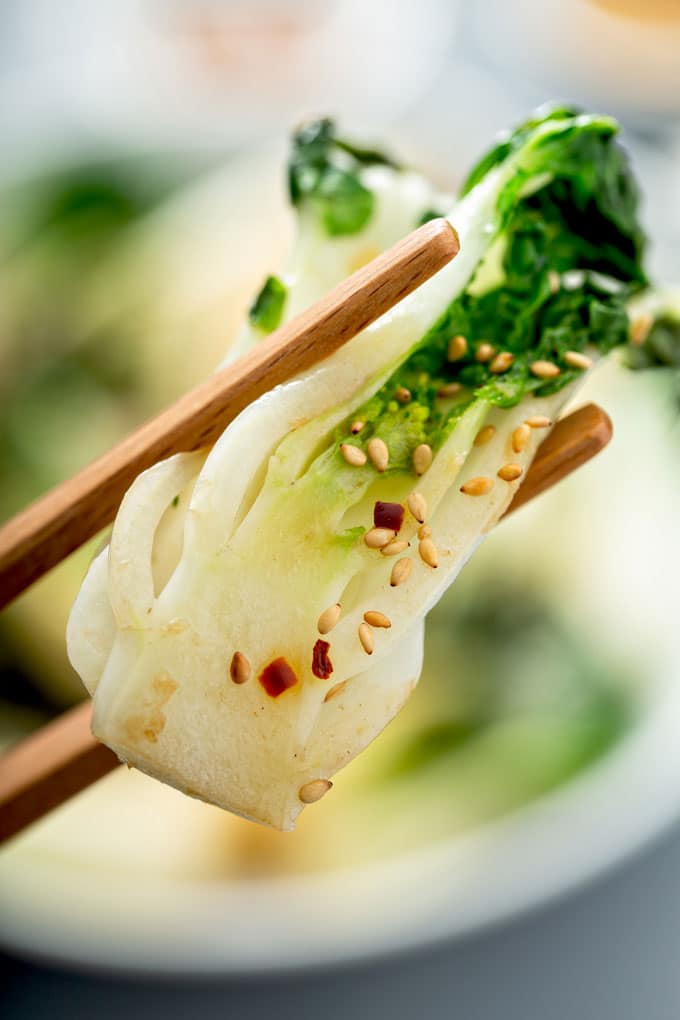 A close-up view of a stir-fried bok choy being held with chopsticks. 