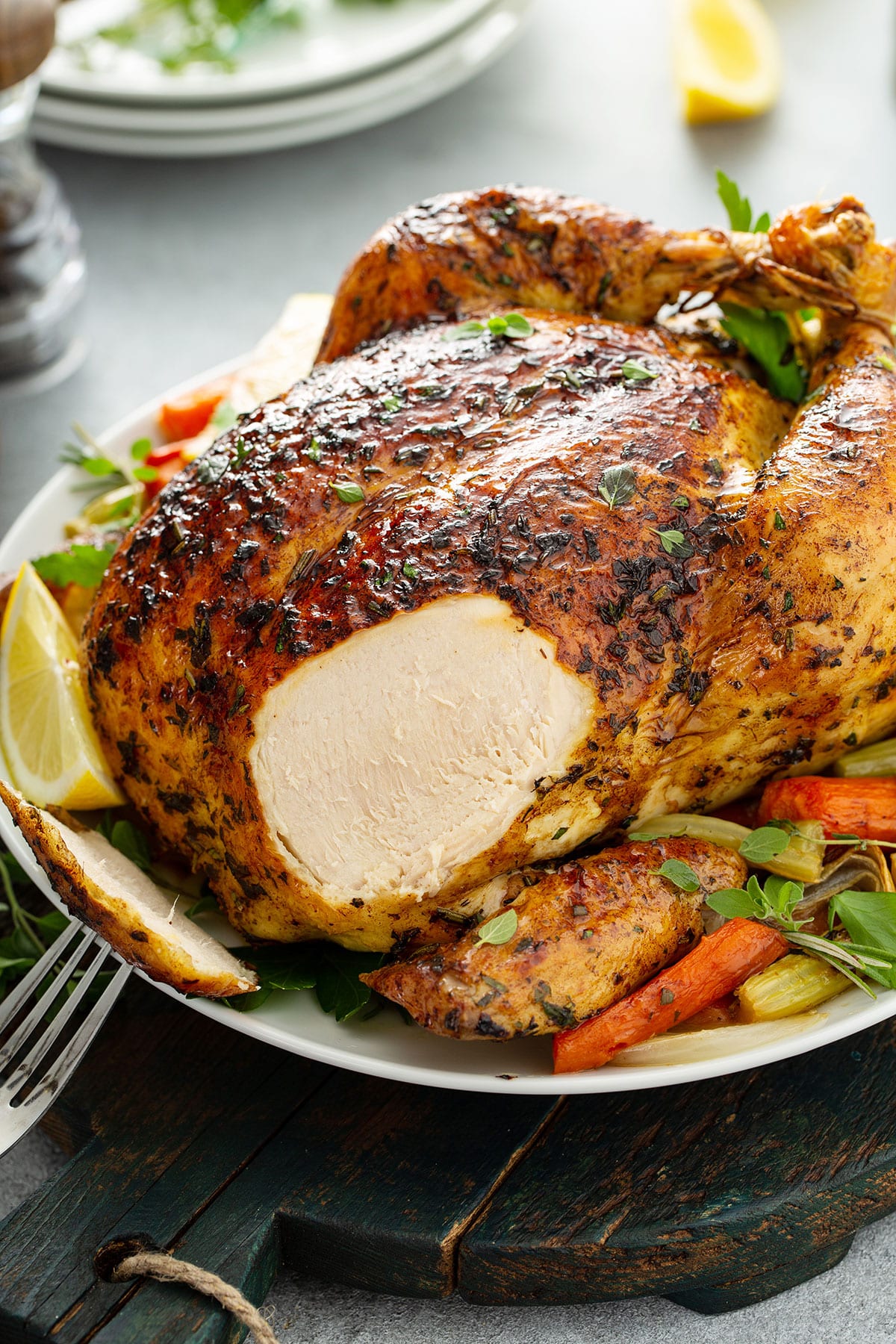 A whole roast chicken with a piece of breast sliced off on a white plate.