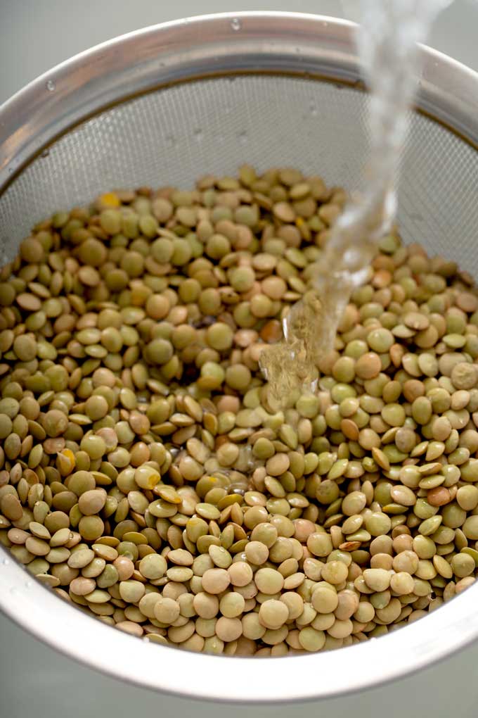 Lentils in a fine mesh sieve getting rinsed under cold water