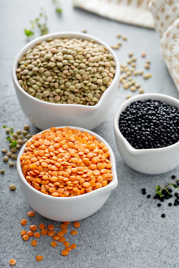 Three white ceramic measuring bowls . One with orange lentils, one with beluga black lentils and one with brown lentils
