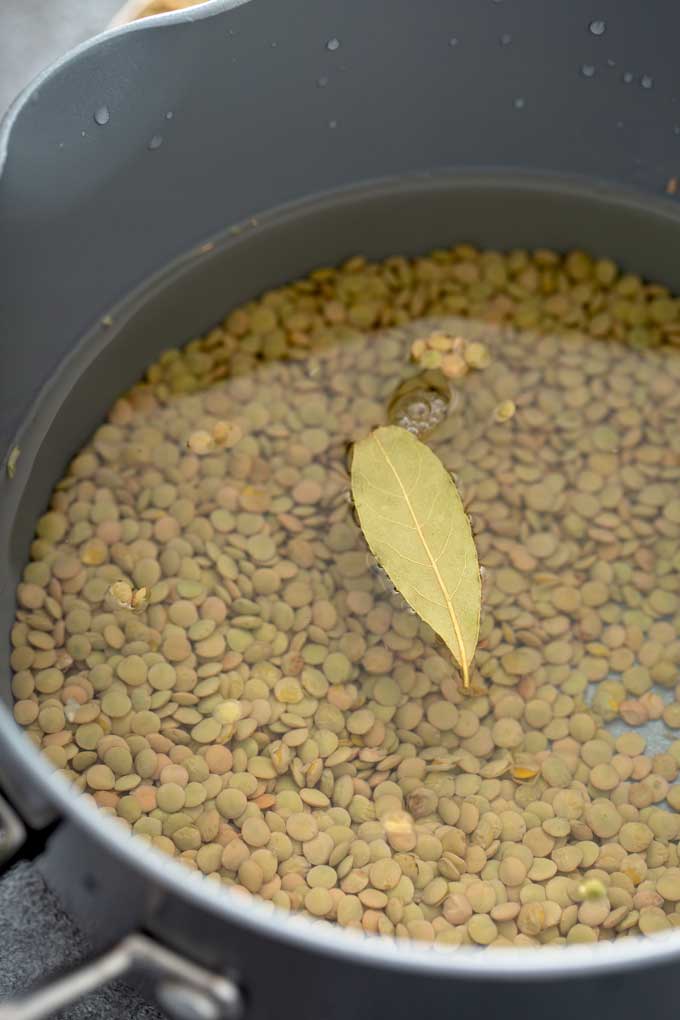 Raw lentils in a pot with water and a bay leaf.