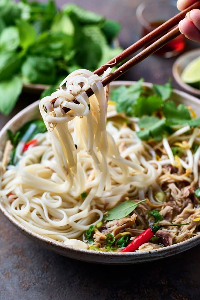 lifting rice noodles with chopsticks from a bowl of pho.