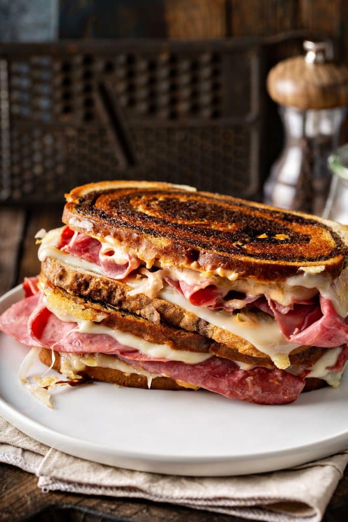 Two grilled Reuben sandwiches, one on top of the other on a white plate