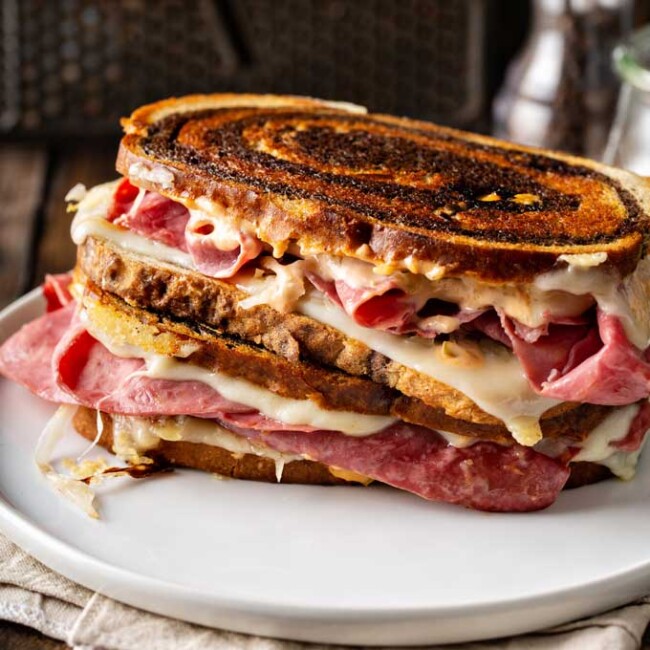Two Reuben sandwiches stacked on a white plate