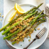 Roasted asparagus with crispy topping on a white plate