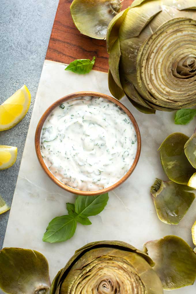 Top view of artichoke dipping sauce in a wooden bowl over a marble board