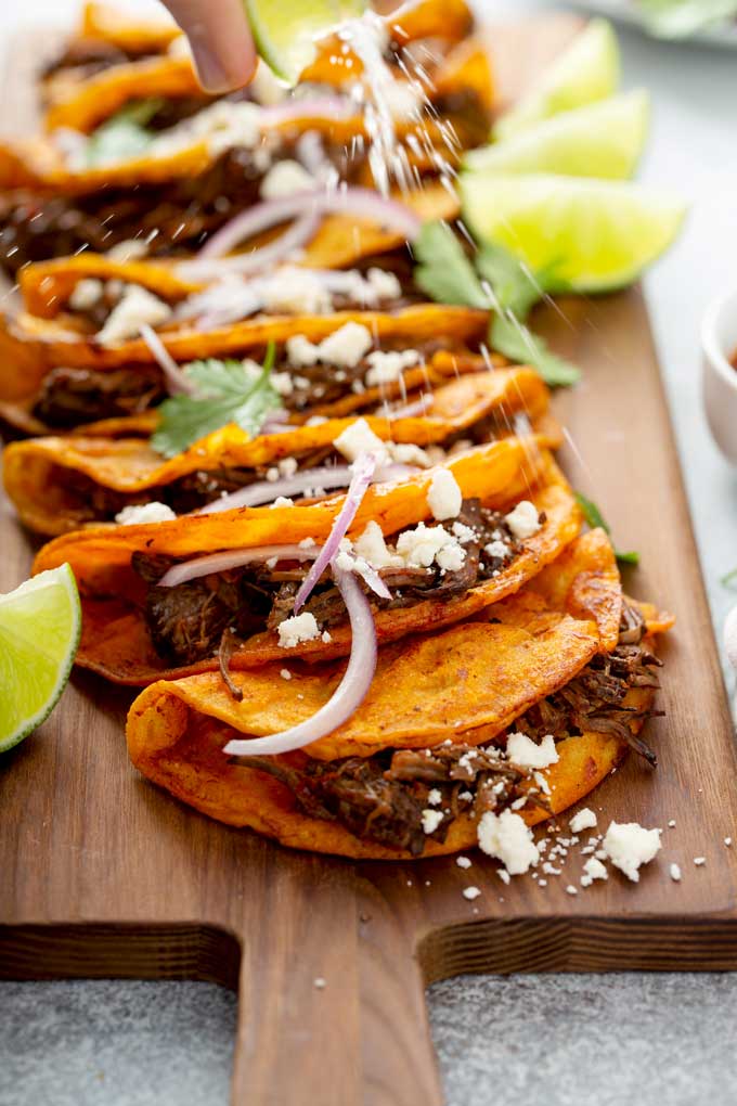 Squeeze of fresh lime juice over shredded beef tacos on a wooden board