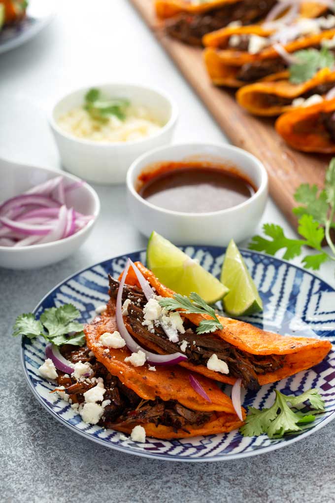 Mexican shredded beef birria tacos on a plate served with onions, cheese and limes