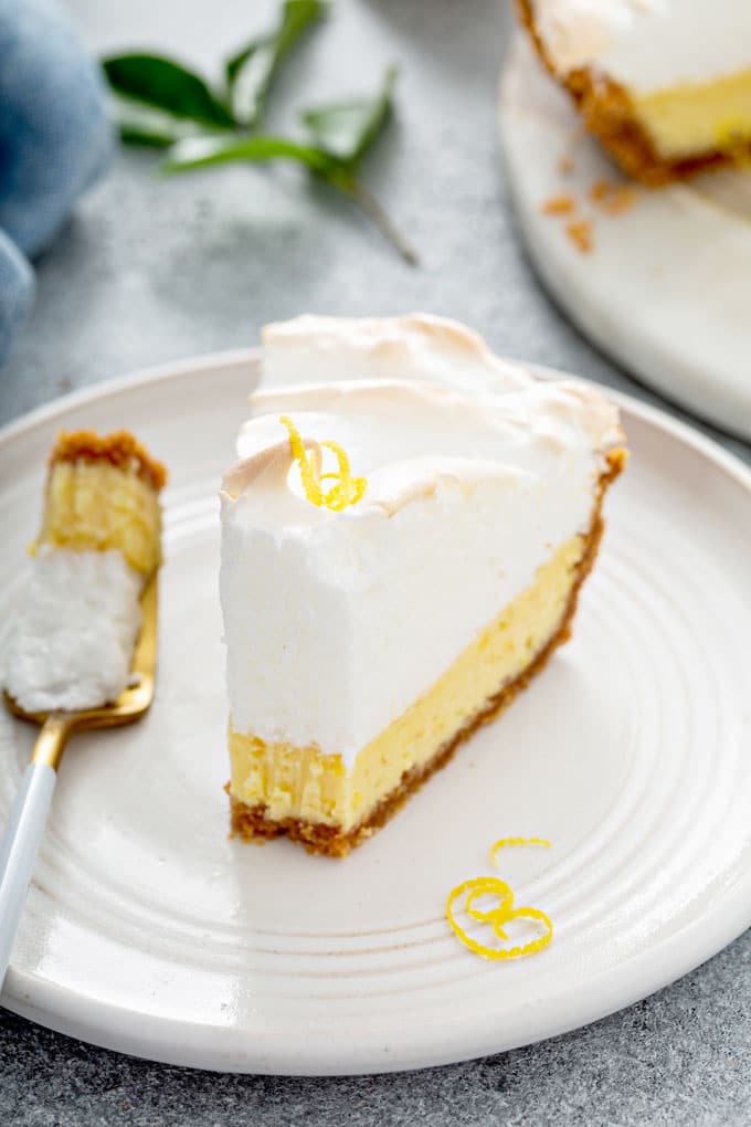Slice of lemon cream pie with a piece taken off on a white plate
