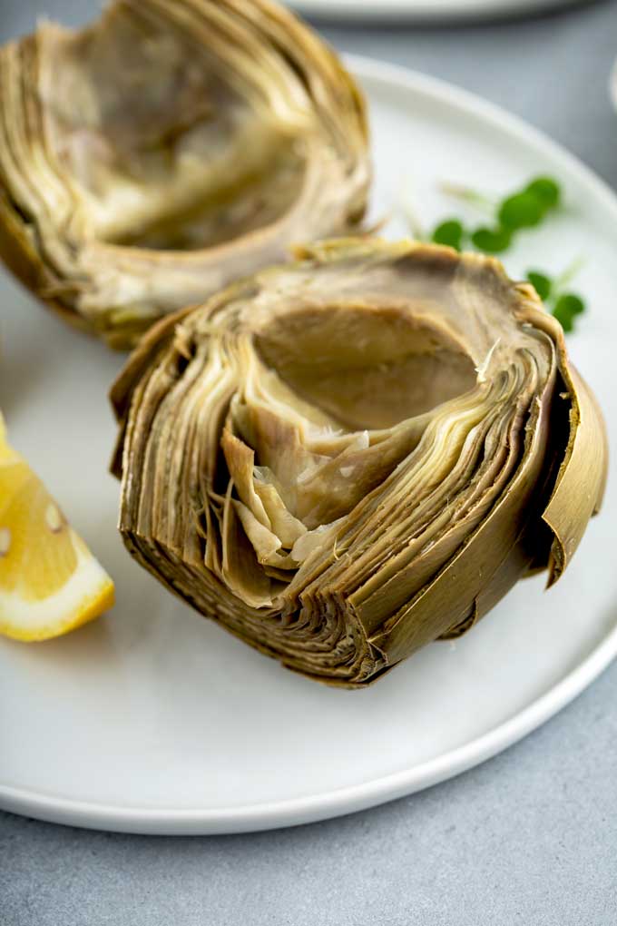 A cooked artichoke cut in half on a white plate.