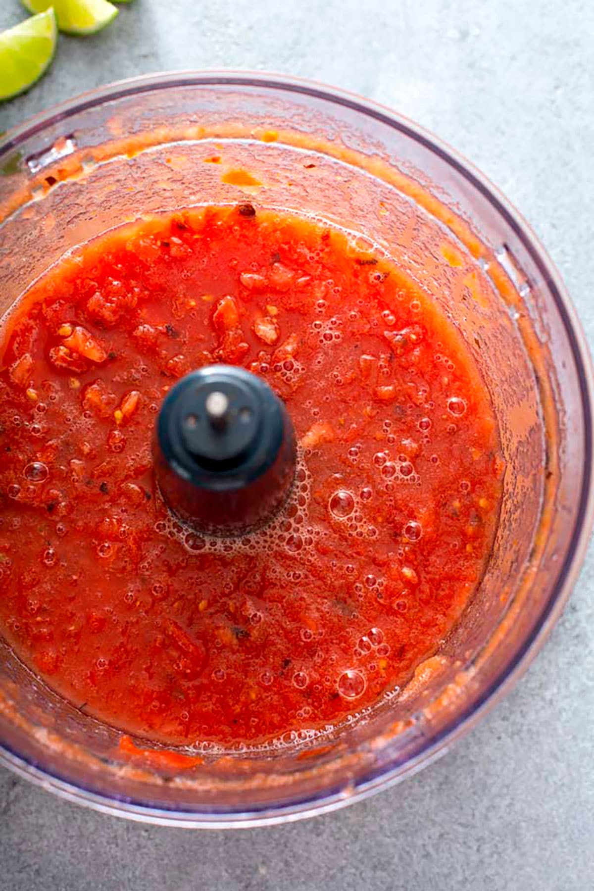 Processed tomatoes and chiles in the bowl of a food processor.
