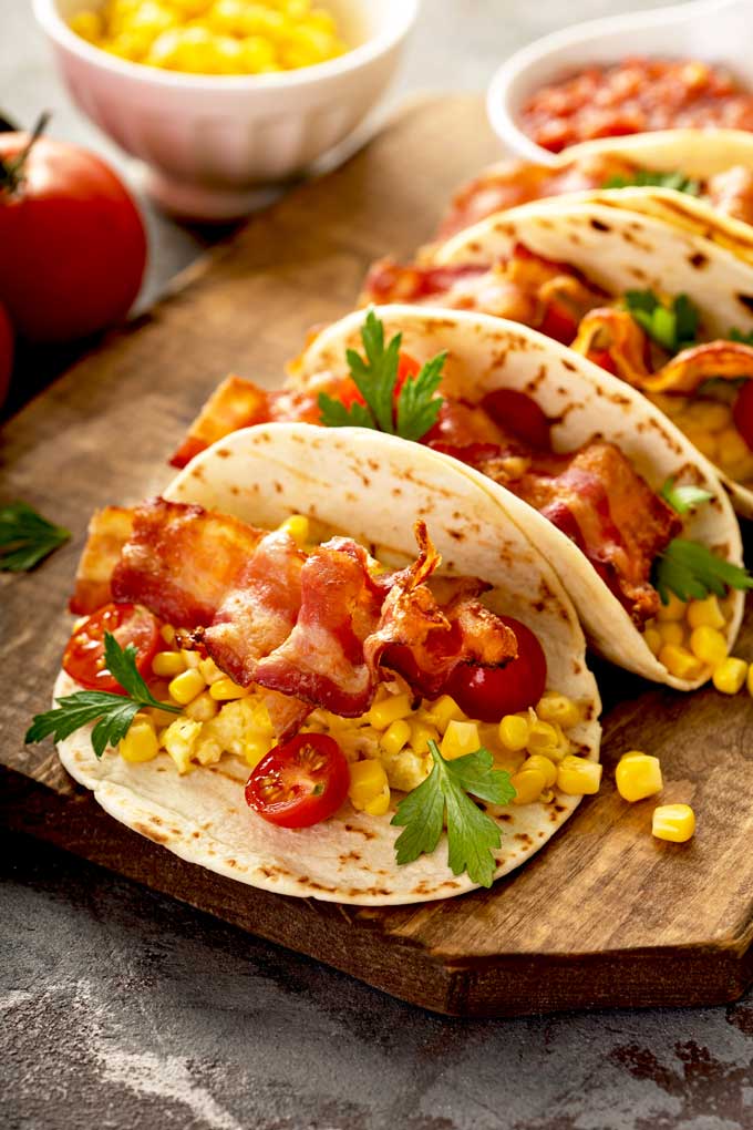 Soft flour tortilla tacos with scrambled eggs, bacon, corn salsa, potatoes and garnishes