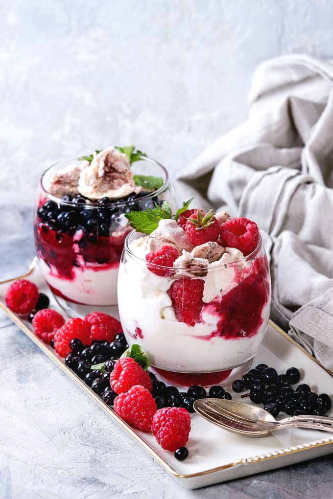 Two glasses filled with whipped cream, crushed meringues and berries