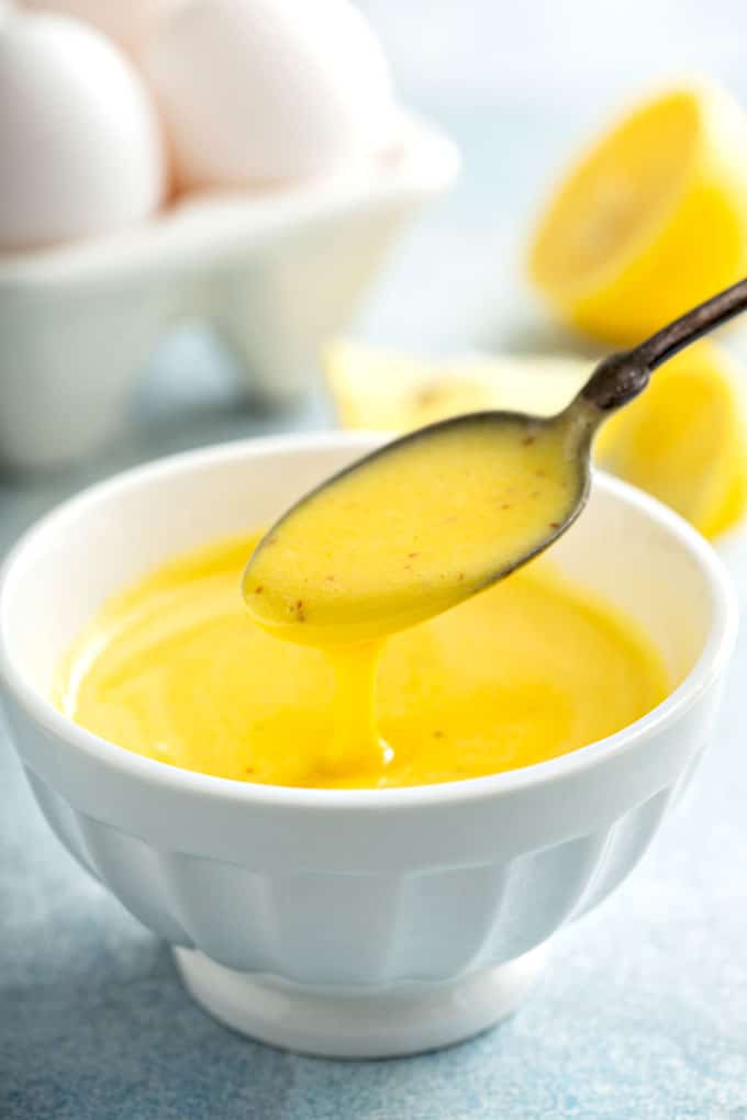 Scooping Hollandaise sauce from a white bowl.