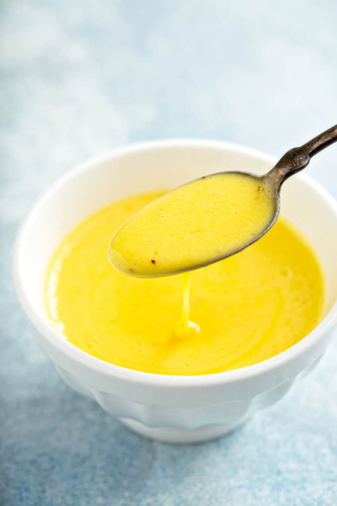 Scooping Hollandaise sauce from a white bowl.
