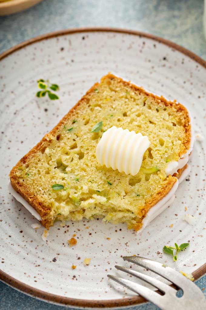 A sliced of zucchini lemon bread topped with a pad of butter on a plate