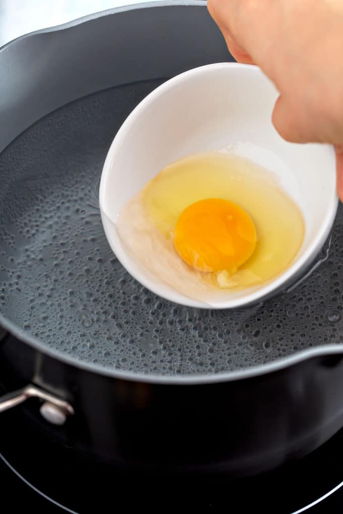 Dropping a raw egg in the simmering water with a small cup