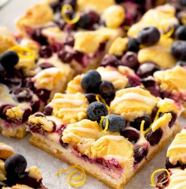 Cut up cheesecake crumb bars with blueberries on parchment paper.