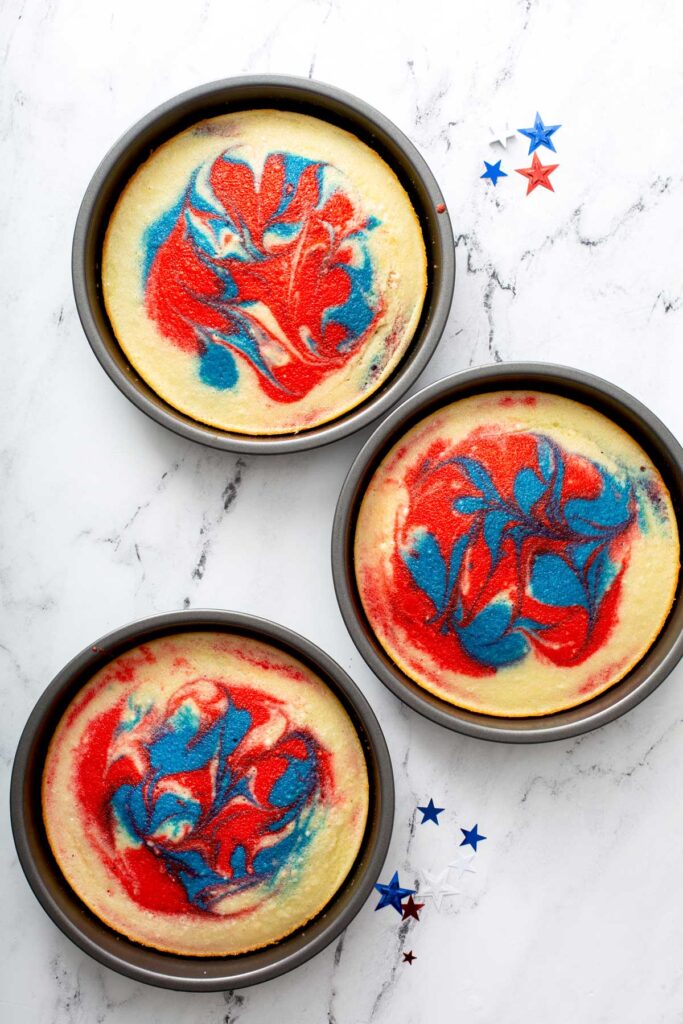 Baked tie dye cakes in baking pans cooling off.