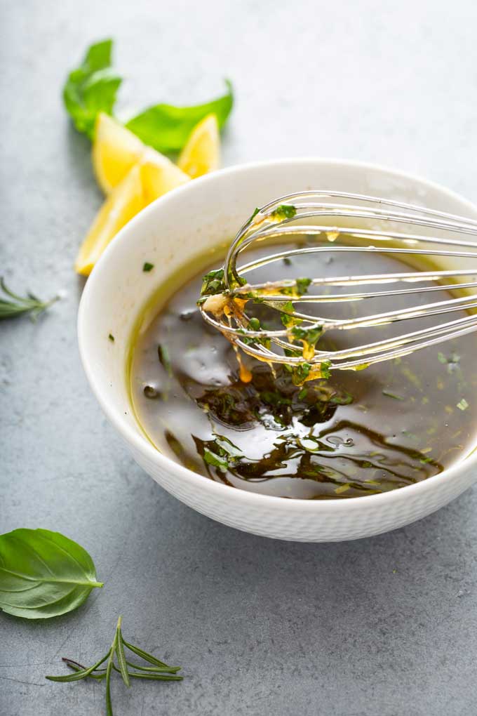 Marinade with balsamic vinegar, fresh garlic and herbs in a white mixing bowl.