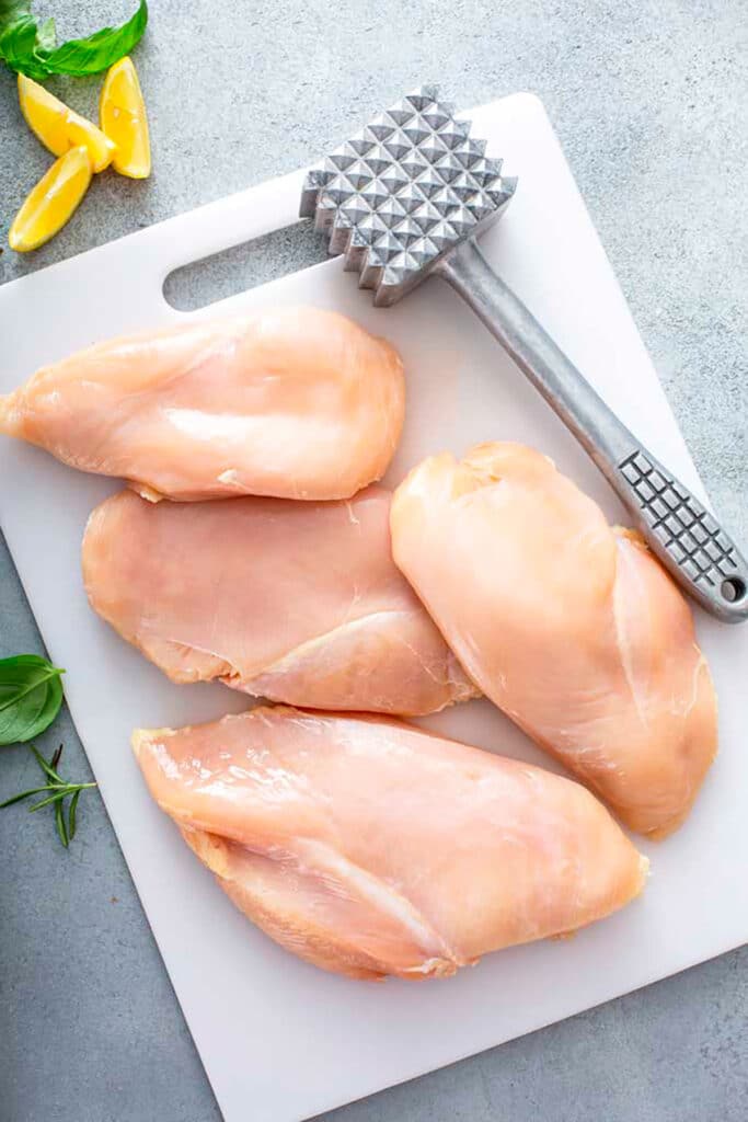 Top view of 4 chicken breasts on a white cutting board 