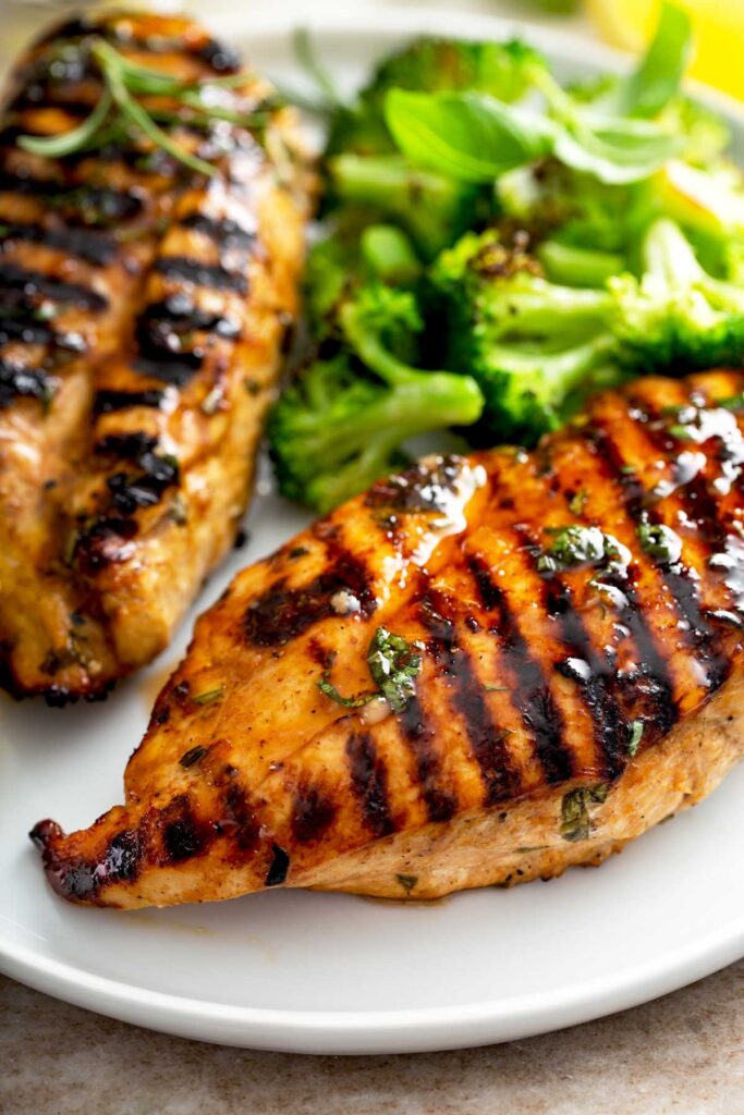 Close view of 2 Grilled Chicken Breasts on a white plate and garnished with chopped broccoli