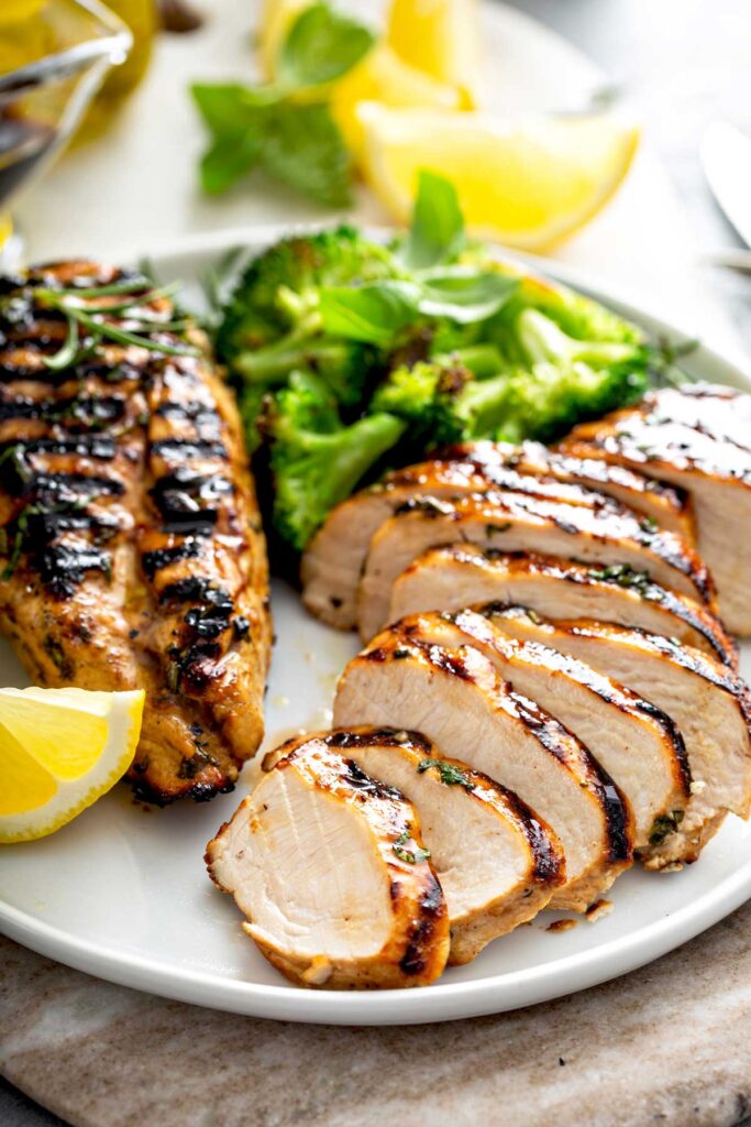 Close view of Grilled Chicken partially sliced and garnished with broccoli and slices of lemon