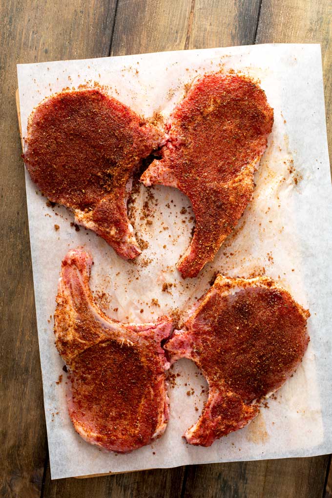Raw bone-in pork chops seasoned with Texas BBQ spice mix on a piece of parchment paper.