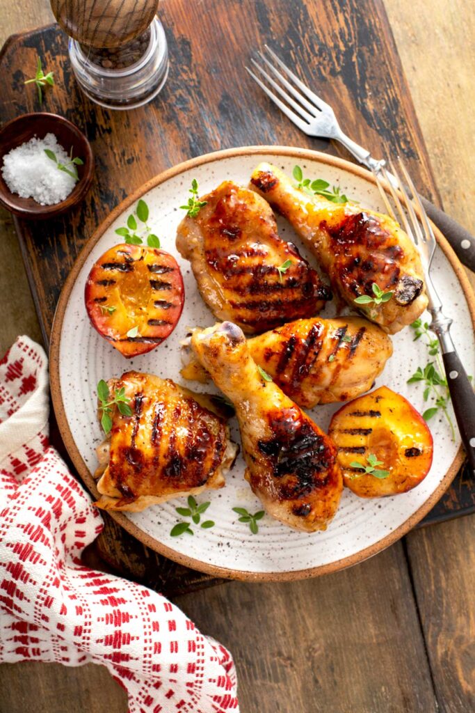 Glazed chicken legs and thighs served on a plate with grilled peaches