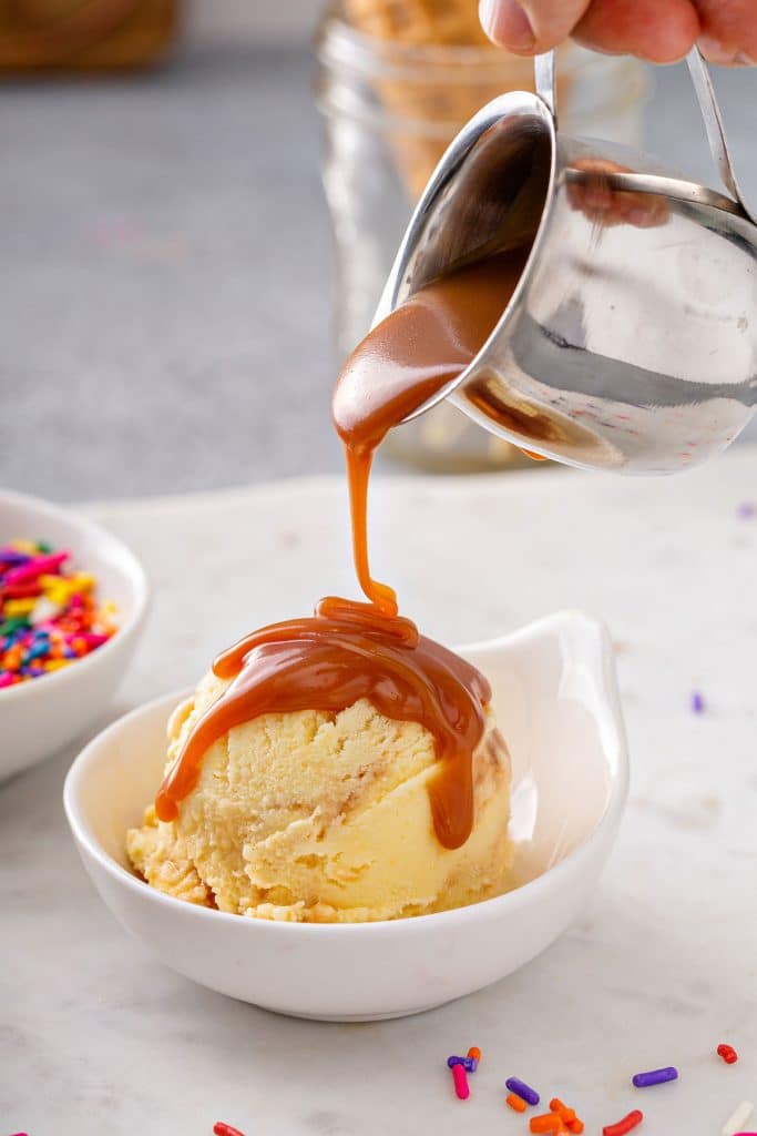 pouring caramel sauce over a scoop of corn ice cream in a small white dish