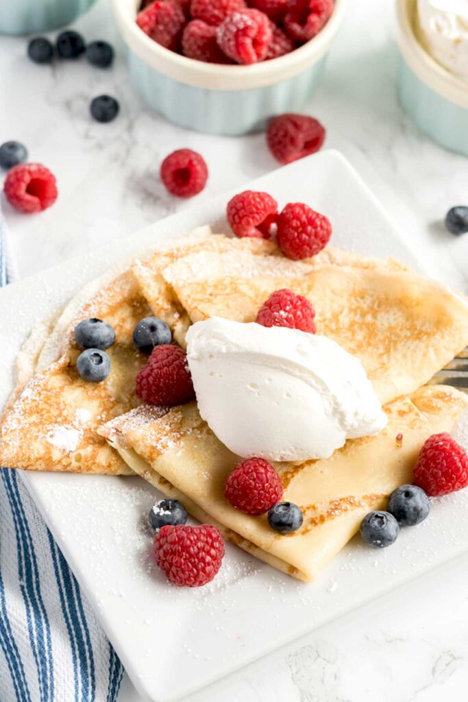 Folded homemade crepes topped with whipped cream and berries.