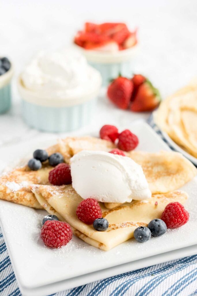 A serving of sweet French pancakes topped with whipped cream and berries.