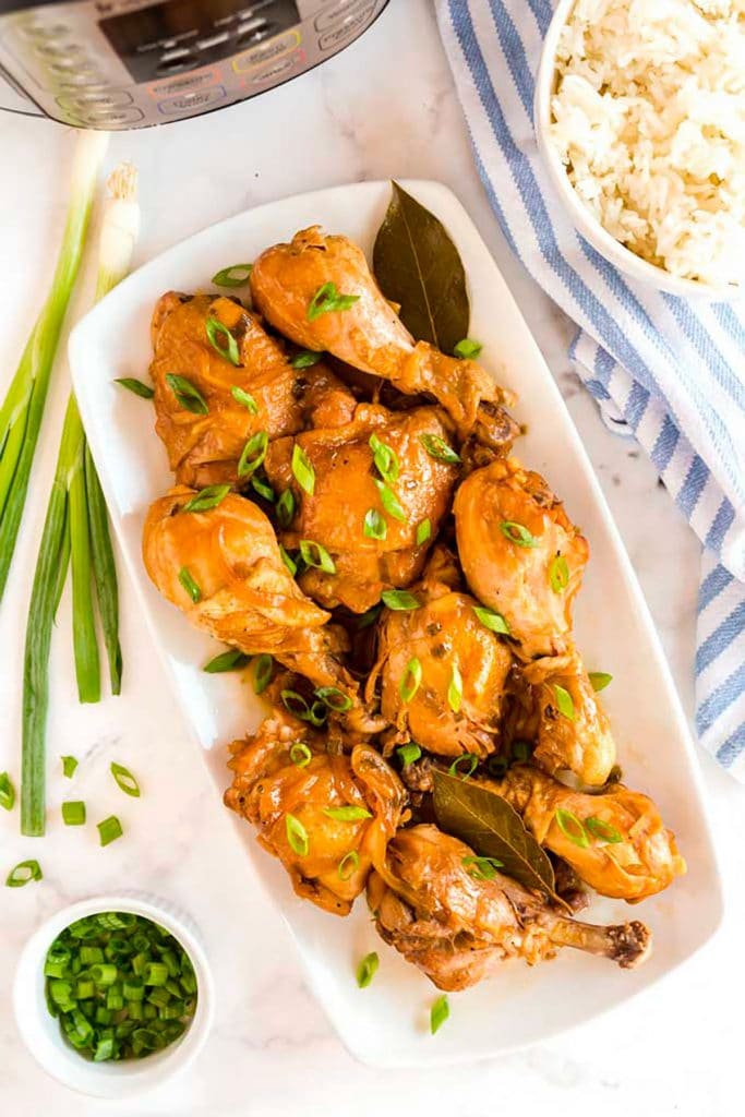 Top view of Chicken Adobo pieces on a long white plate, decorated with chopped green onion and bay leaves.