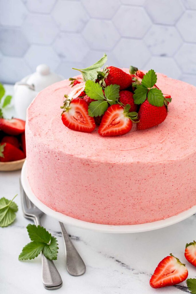 A whole frosted strawberry cake topped with fresh strawberries