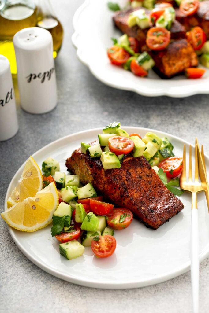 Blackened salmon recipe with a fresh cucumber tomato and avocado salad served on a white plate