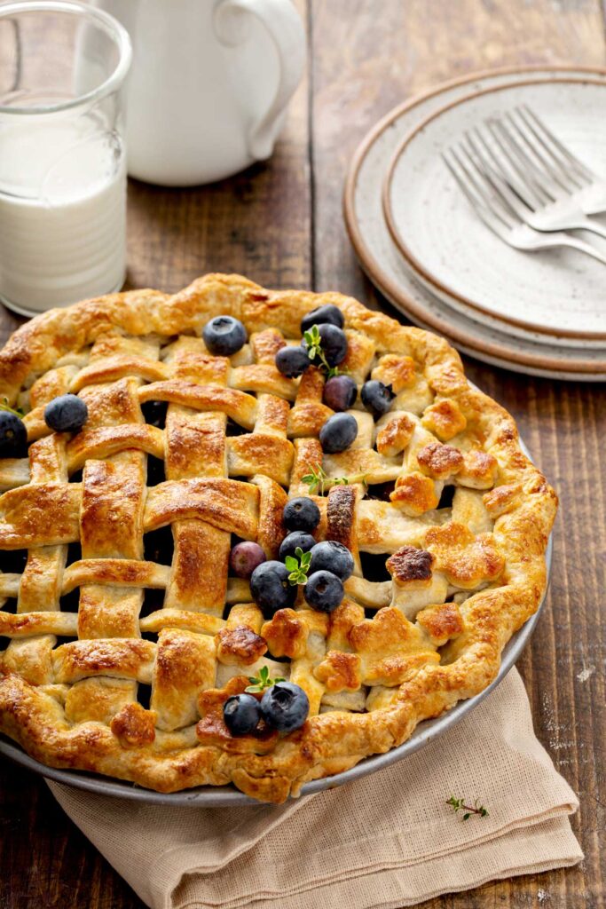 A whole blueberry pie with a lattice golden brown pie crust and some blueberries on top